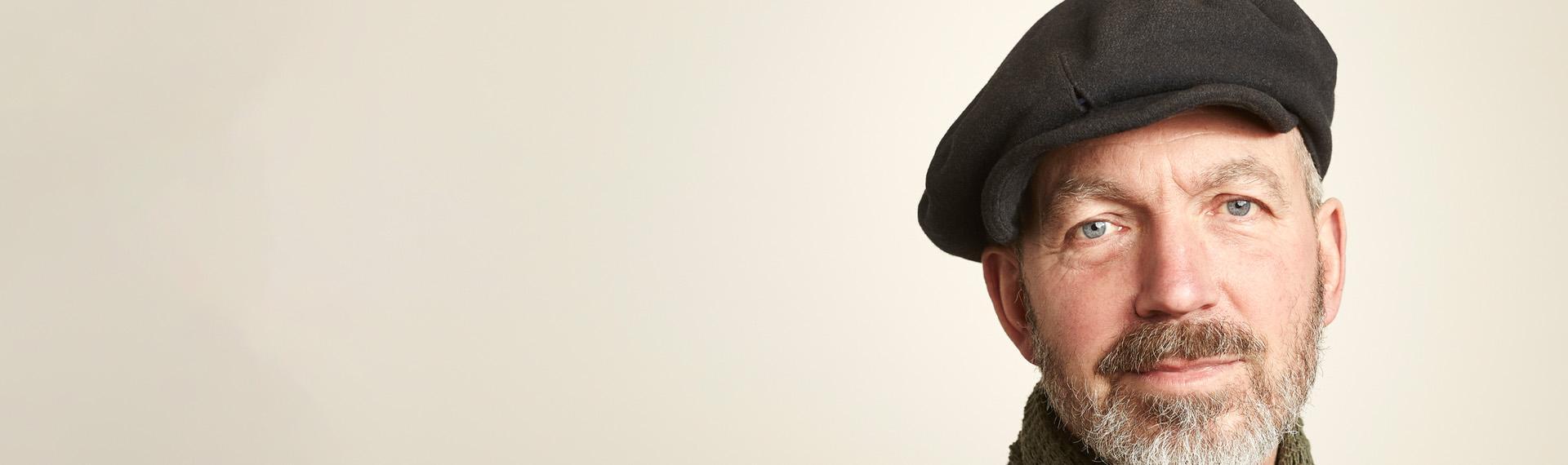 Starszy mężczyzna w kaszkiecie na beżowym tle